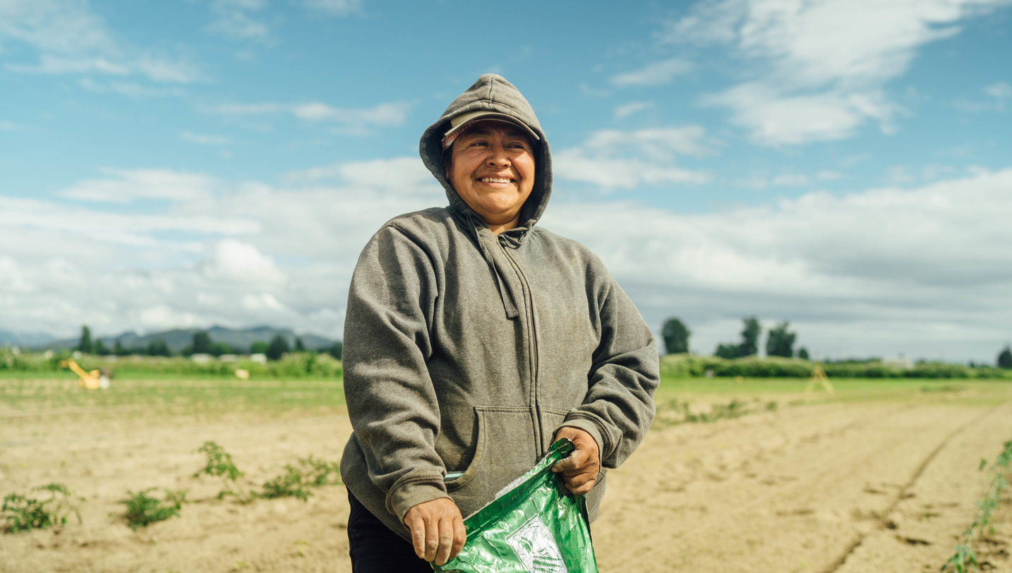 A smiling woman holding a bag of soil and ready to garden