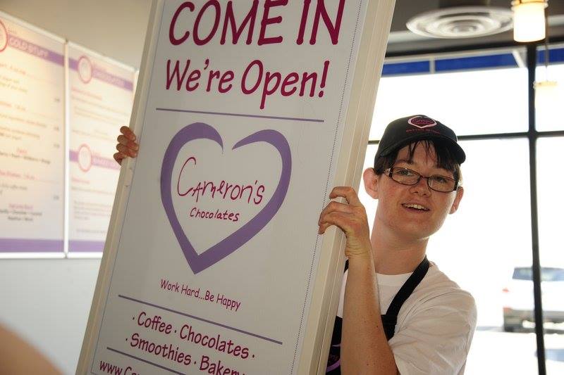 Friendly employee holding up a Cameron's Chocolates display sign, encouraging people to come in