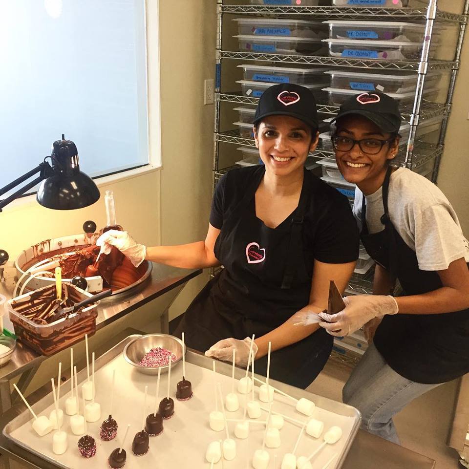 Two female employees share a smile while making chocolate covered marshmallows with sprinkles