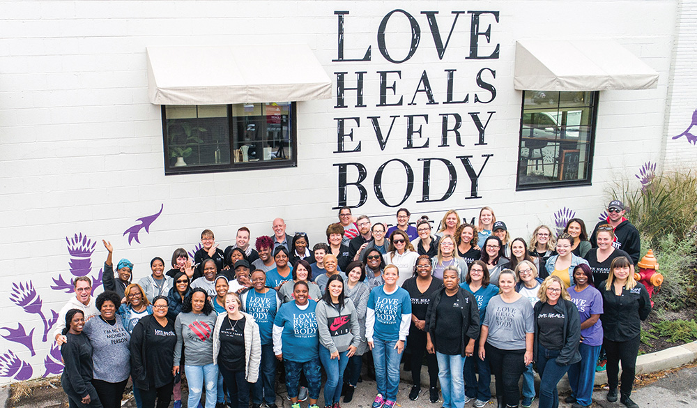 Thistle Farms team posing in front of mural saying Love Heals Everybody