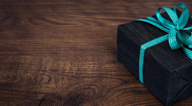 A gift wrapped in black wrapping paper with an aqua blue bow, placed on a wooden table.