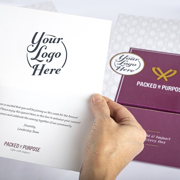 Close-up of a hand holding a brandable note included in a Packed with Purpose gift box