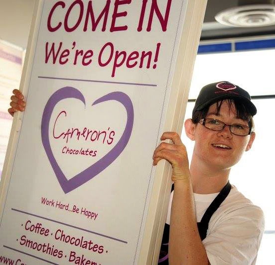 Young woman carrying a Cameron's sign saying "Come on it, we're open!"