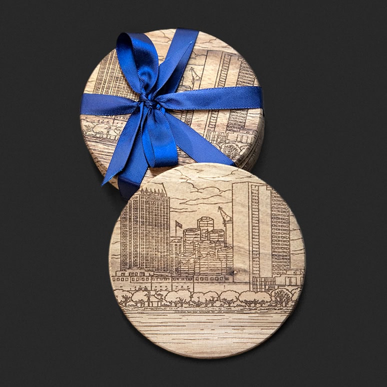 A set of coasters with an engraved cityscape wrapped in blue ribbon